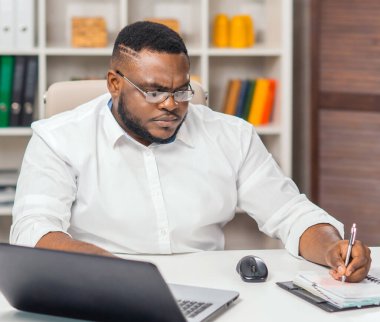 Ofisteki işyerinde. Genç Afro-Amerikalı bir adam bilgisayar ve diğer cihazları kullanarak çalışıyor. Uzak görev kavramı.