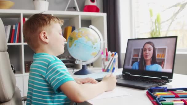 Boy fait ses devoirs à la table. Cute Child apprend à la maison à l'aide d'ordinateurs portables et de manuels scolaires. Concept d'étude et d'enseignement à distance. — Video