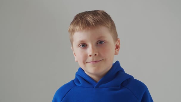 Retrato de menino sorridente feliz em camiseta azul. Criança atraente em estúdio sobre cinza. — Vídeo de Stock