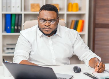 Ofisteki işyerinde. Genç Afro-Amerikalı bir adam bilgisayar ve diğer cihazları kullanarak çalışıyor. Uzak görev kavramı.