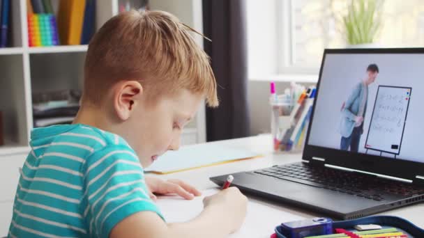 A fiú épp a házi feladatát végzi az asztalnál. Aranyos gyermek tanul otthon segítségével Laptop Számítógép és iskolai tankönyvek. Tanulmányi és távoktatási koncepció. — Stock videók