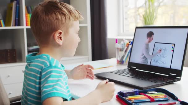 Pojken gör sina läxor vid bordet. Söta barn är att lära sig hemma med hjälp av bärbar dator och läroböcker skola. Studie- och distansutbildningskoncept. — Stockvideo