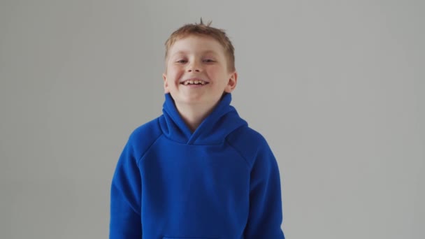 Porträt eines glücklich lächelnden Jungen im blauen T-Shirt. Attraktives Kind im Studio über grau. — Stockvideo