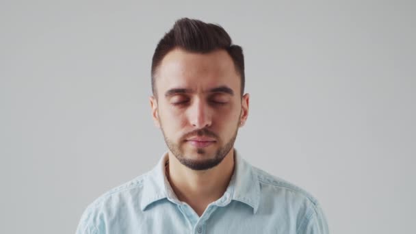 El joven caucásico Brunet Man está mirando a la cámara sobre un fondo gris claro. Estudio retrato facial masculino. Luz natural del día. — Vídeos de Stock