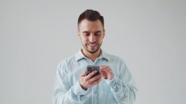 Akıllı Telefon Cihazı ile Kafkas Sakallı Genç Adam Açık Gri Arkaplanda Kameraya Bakıyor. Stüdyo Erkek Yüz Portresi. Doğal Gün Işığı.