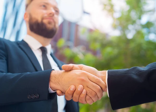 Handshake close-up. Businessman and his colleague are shaking hands in front of modern office building. Financial investors outdoor. Banking and business.