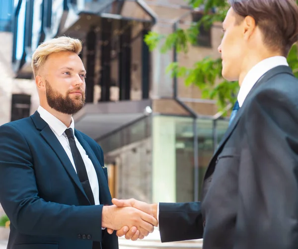 Handshake close-up. Businessman and his colleague are shaking hands in front of modern office building. Financial investors outdoor. Banking and business.