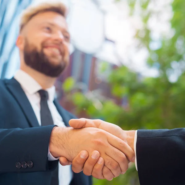 Handshake close-up. Businessman and his colleague are shaking hands in front of modern office building. Financial investors outdoor. Banking and business.
