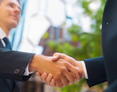 Kendine güvenen işadamı ve meslektaşı modern ofis binasının önünde el sıkışıyorlar. Finansal yatırımcılar açık havada. Bankacılık ve iş konsepti.