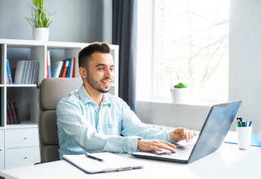 Young Man Works while Sitting in front of a Computer at Home. The Workplace of a Professional Worker, Freelancer or Student. The Concept of Distance Work and Education.