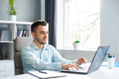 Genç adam evde bir bilgisayarın önünde otururken çalışıyor. Profesyonel bir işçinin, serbest çalışanın ya da öğrencinin işyeri. Mesafe Çalışma ve Eğitim Konsepti.