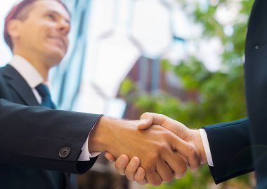Kendine güvenen işadamı ve meslektaşı modern ofis binasının önünde el sıkışıyorlar. Finansal yatırımcılar açık havada. Bankacılık ve iş konsepti.