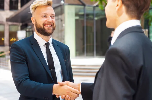 Handshake close-up. Businessman and his colleague are shaking hands in front of modern office building. Financial investors outdoor. Banking and business.