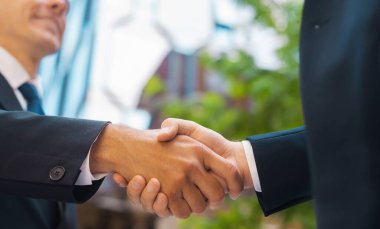 Kendine güvenen işadamı ve meslektaşı modern ofis binasının önünde el sıkışıyorlar. Finansal yatırımcılar açık havada. Bankacılık ve iş konsepti.