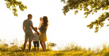 Mutlu sevgi dolu aile gün batımında dışarıda yürüyor. Baba, anne, oğul ve kız. Deniz ve alan arkaplanı