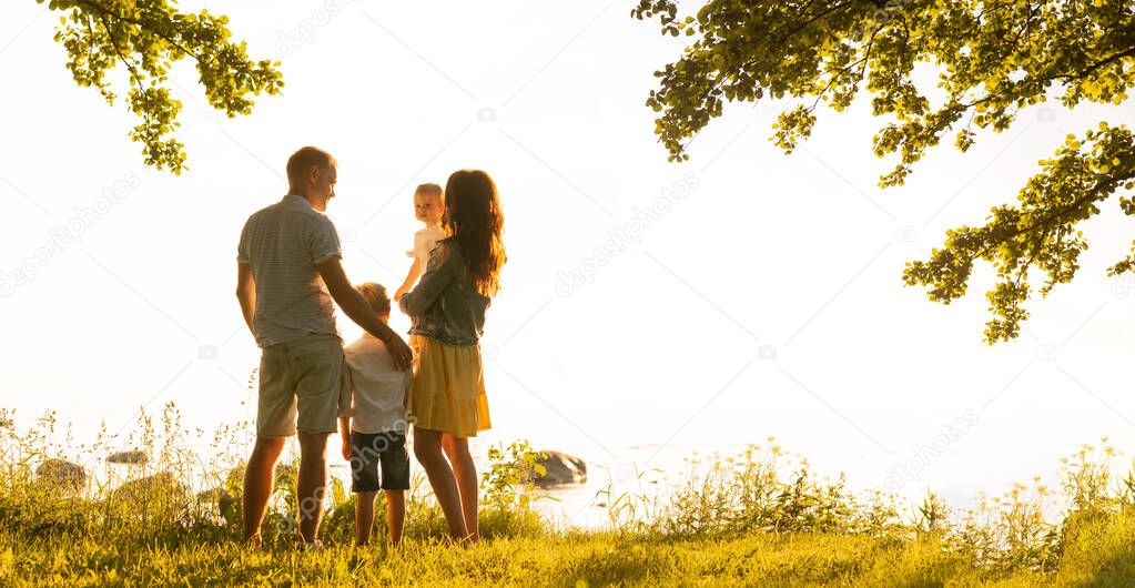 Happy loving family walking outdoor in the light of sunset. Father, mother, son and daughter. Sea and field background