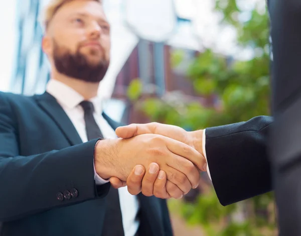 Handshake close-up. Businessman and his colleague are shaking hands in front of modern office building. Financial investors outdoor. Banking and business.