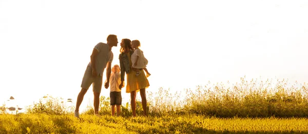 Mutlu sevgi dolu aile gün batımında dışarıda yürüyor. Baba, anne, oğul ve kız. Deniz ve alan arkaplanı