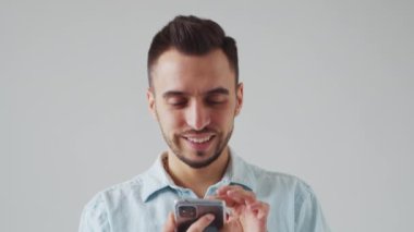 Akıllı Telefon Cihazı ile Kafkas Sakallı Genç Adam Açık Gri Arkaplanda Kameraya Bakıyor. Stüdyo Erkek Yüz Portresi. Doğal Gün Işığı.