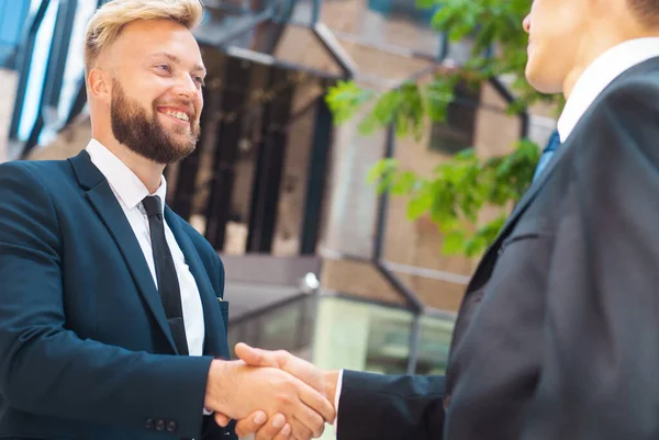 Handshake close-up. Businessman and his colleague are shaking hands in front of modern office building. Financial investors outdoor. Banking and business.