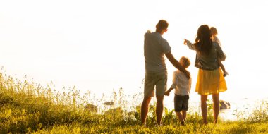 Mutlu sevgi dolu aile gün batımında dışarıda yürüyor. Baba, anne, oğul ve kız. Deniz ve alan arkaplanı