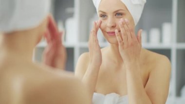 Genç Kız, Tuvalette Makyaj Aynası 'nın önünde oturuyor ve cilt kremi sürüyor. Güzel kadın kozmetik yenileme prosedürleri uyguluyor. Sağlık ve Güzellik Konsepti.