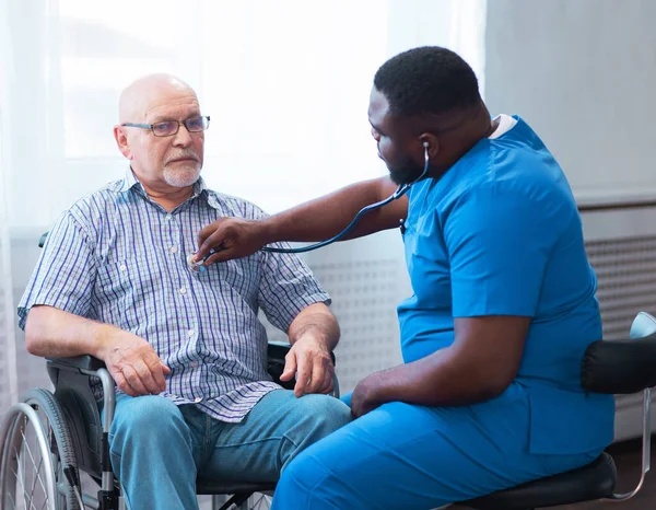 Professional doctor helps an elderly man with chronic diseases. Therapist and patient in home interior. The concept of health care and medicine.