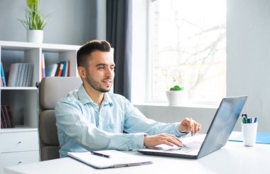 Genç adam evde bir bilgisayarın önünde otururken çalışıyor. Profesyonel bir işçinin, serbest çalışanın ya da öğrencinin işyeri. Mesafe Çalışma ve Eğitim Konsepti.