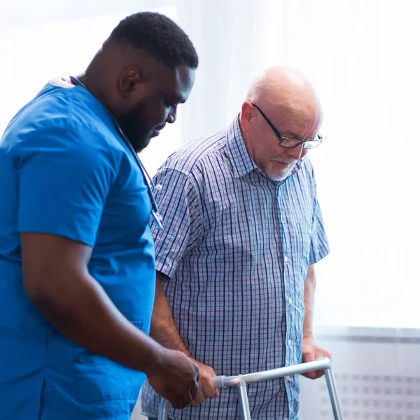 Professional doctor helps an elderly man with chronic diseases. Therapist and patient in home interior. The concept of health care and medicine.