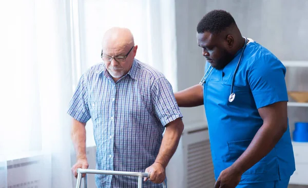 Professional doctor helps an elderly man with chronic diseases. Therapist and patient in home interior. The concept of health care and medicine.