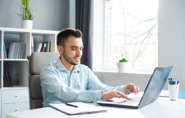 Genç adam evde bir bilgisayarın önünde otururken çalışıyor. Profesyonel bir işçinin, serbest çalışanın ya da öğrencinin işyeri. Mesafe Çalışma ve Eğitim Konsepti.