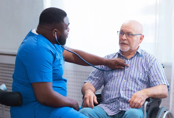 Professional doctor helps an elderly man with chronic diseases. Therapist and patient in home interior. The concept of health care and medicine.