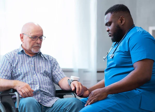 Professional doctor helps an elderly man with chronic diseases. Therapist and patient in home interior. The concept of health care and medicine.