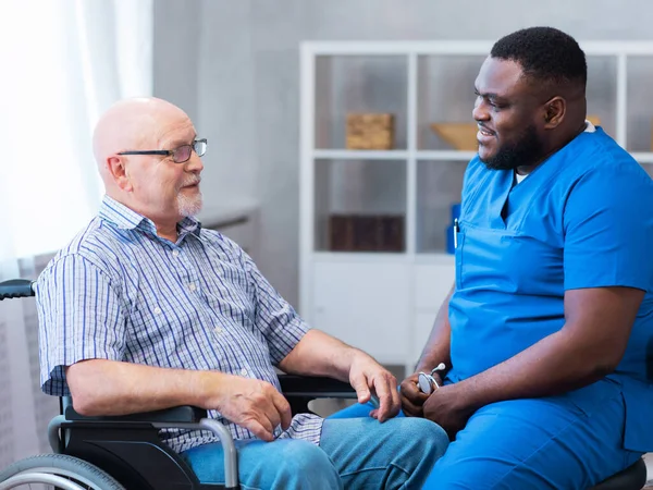 Professional doctor helps an elderly man with chronic diseases. Therapist and patient in home interior. The concept of health care and medicine.