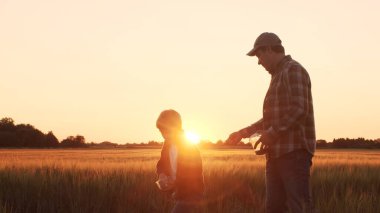 Farmer and his son in front of a sunset agricultural landscape. Man and a boy in a countryside field. The concept of fatherhood, country life, farming and country lifestyle.