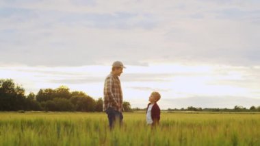 Farmer and his son in front of a sunset agricultural landscape. Man and a boy in a countryside field. The concept of fatherhood, country life, farming and country lifestyle.
