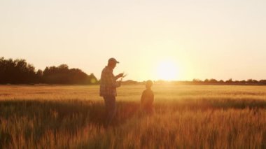 Farmer and his son in front of a sunset agricultural landscape. Man and a boy in a countryside field. The concept of fatherhood, country life, farming and country lifestyle.