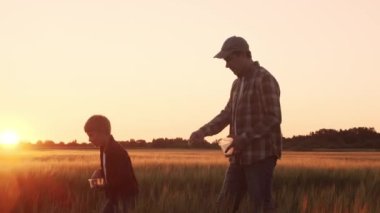 Farmer and his son in front of a sunset agricultural landscape. Man and a boy in a countryside field. The concept of fatherhood, country life, farming and country lifestyle.