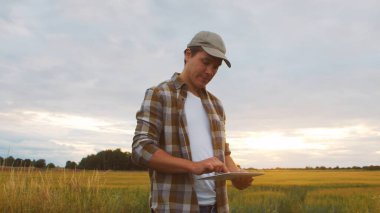 Günbatımı tarım manzarasının önünde tablet bilgisayarlı bir çiftçi. Kırsal kesimde bir adam. Kır hayatı, gıda üretimi, tarım ve teknoloji kavramı.