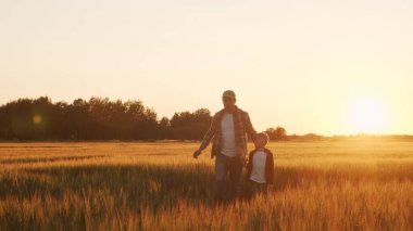 Farmer and his son in front of a sunset agricultural landscape. Man and a boy in a countryside field. The concept of fatherhood, country life, farming and country lifestyle.