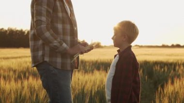 Farmer and his son in front of a sunset agricultural landscape. Man and a boy in a countryside field. The concept of fatherhood, country life, farming and country lifestyle.