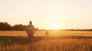 Farmer and his son in front of a sunset agricultural landscape. Man and a boy in a countryside field. The concept of fatherhood, country life, farming and country lifestyle.