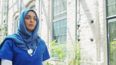 Professional Muslim medical doctor works in front of hospital office. Portrait of young and attractive Middle Eastern female physician in hijab. Medical concept.