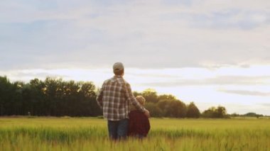 Farmer and his son in front of a sunset agricultural landscape. Man and a boy in a countryside field. The concept of fatherhood, country life, farming and country lifestyle.