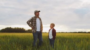 Çiftçi ve oğlu günbatımı tarımının önünde. Kırsalda bir adam ve bir çocuk. Babalık kavramı, köy hayatı, tarım ve kırsal yaşam tarzı..