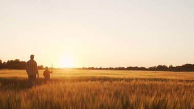 Farmer and his son in front of a sunset agricultural landscape. Man and a boy in a countryside field. The concept of fatherhood, country life, farming and country lifestyle.