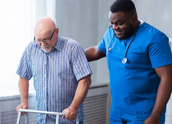 Professional doctor helps an elderly man with chronic diseases. Therapist and patient in home interior. The concept of health care and medicine.