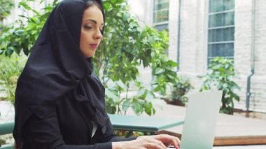 Portrait of young and confident Muslim business woman with a laptop in hijab. Middle Eastern office worker or businesswoman is working outdoor in the city. Corporate and financial concept.