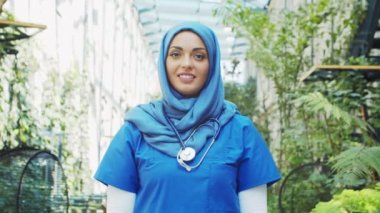 Professional Muslim medical doctor works in front of hospital office. Portrait of young and attractive Middle Eastern female physician in hijab. Medical concept.