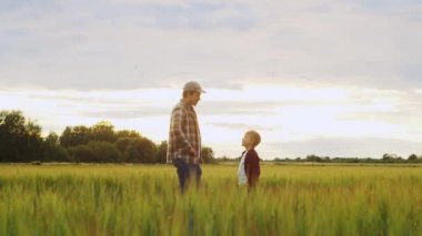 Farmer and his son in front of a sunset agricultural landscape. Man and a boy in a countryside field. The concept of fatherhood, country life, farming and country lifestyle.